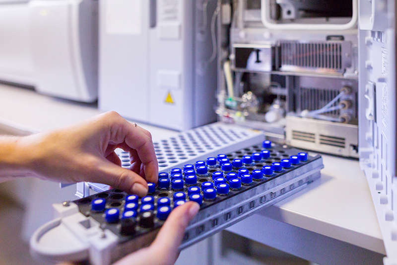 A researcher's hands are seen removing a sample vial from a tray.