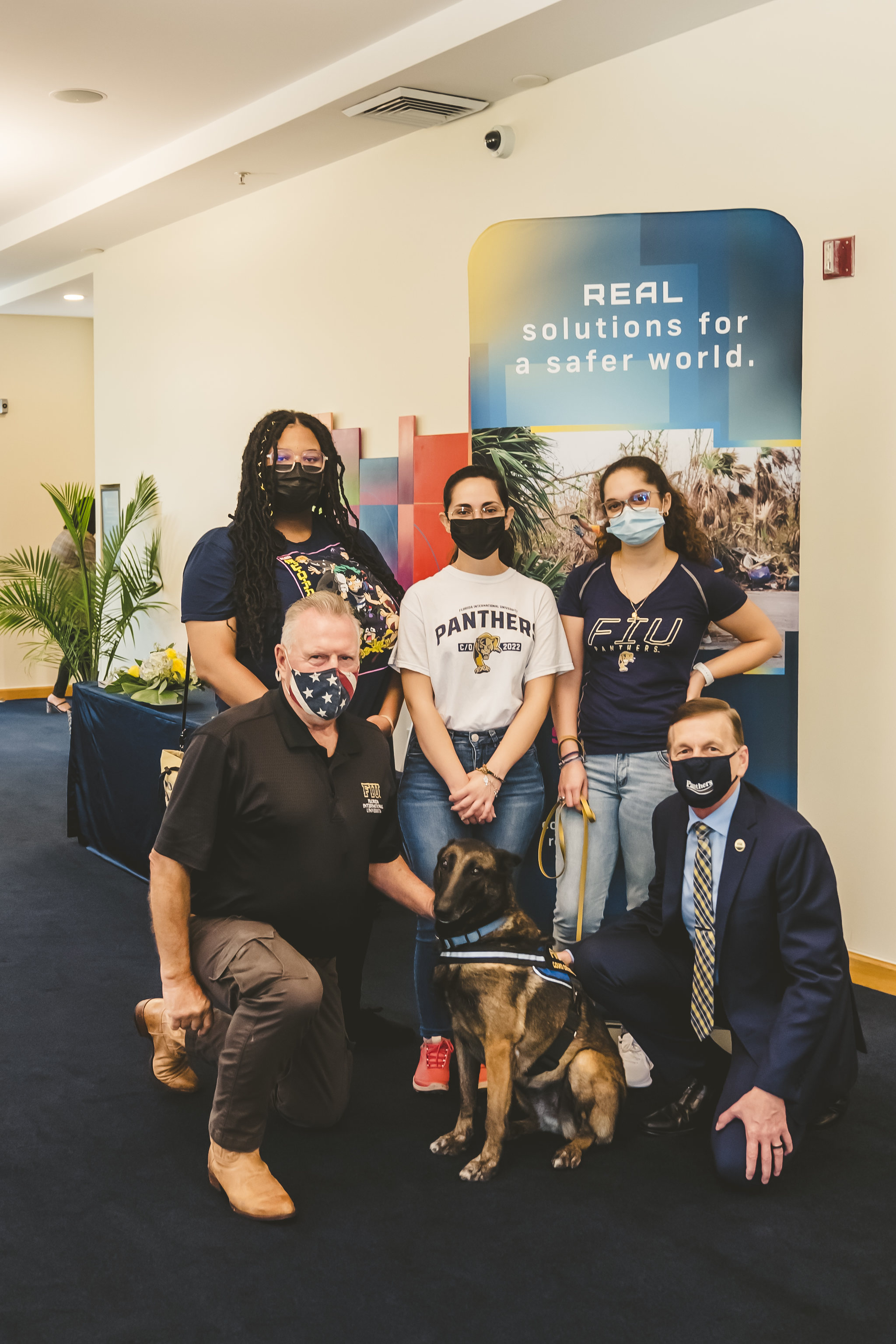 A detection dog, Cobra, sits surrounded by FIU staff and students.