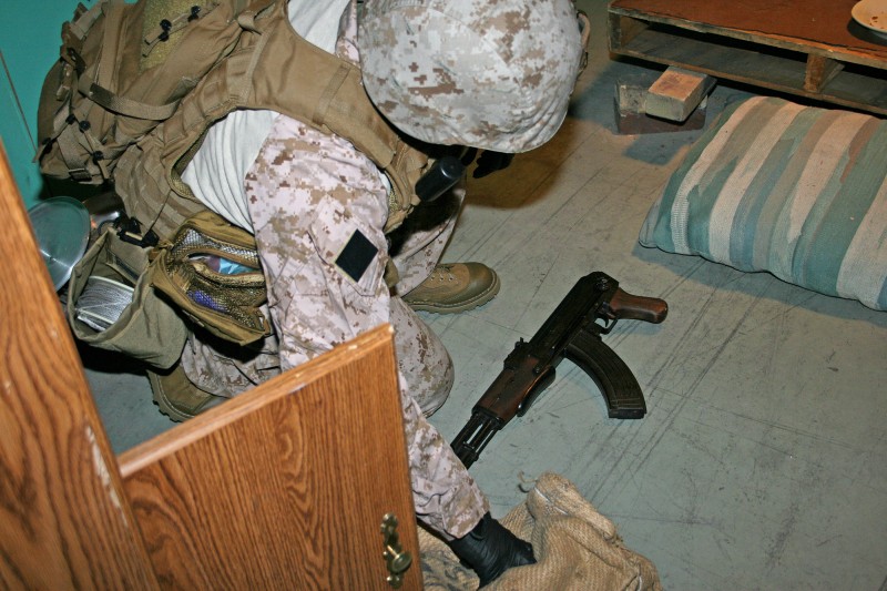 A U.S. military trainee collects a replica weapon during a simulated crime scene scenario.